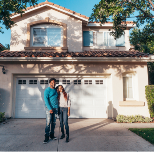 Ethnic couple standing in front of a suburban home.